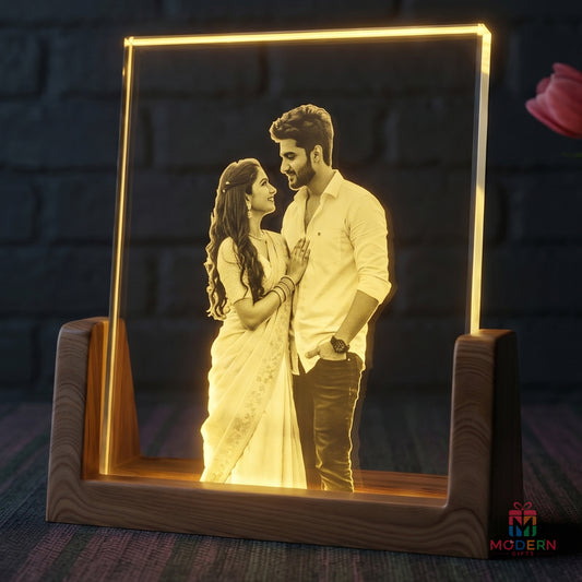 A personalized LED acrylic picture frame on a wooden stand, displaying a romantic couple portrait illuminated in warm yellow light against a dark brick wall background.