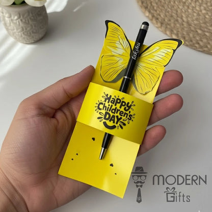 Yellow butterfly-shaped pen holder with a pen, held by a hand, on a white surface with 'Modern Gifts' branding.