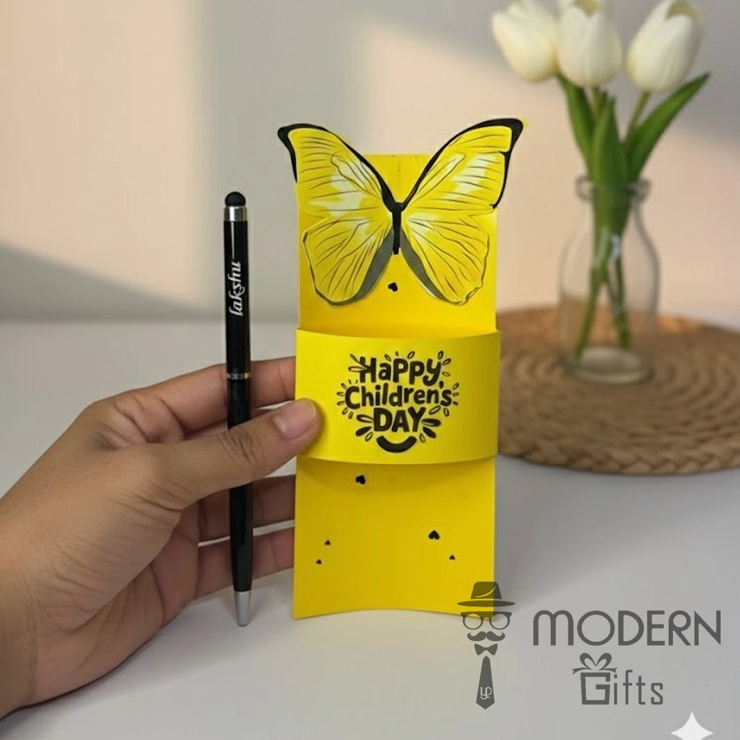 Yellow butterfly-shaped card with 'Happy Children's Day' text held by a hand, with a pen and vase in the background.